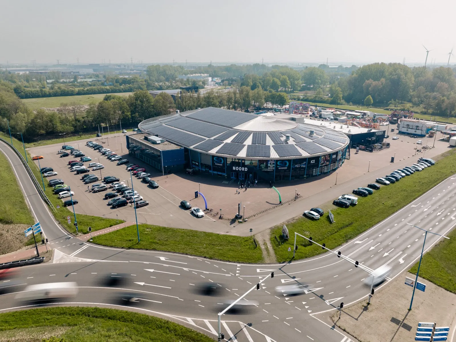 Luchtfoto van het gebouw van SilverDome, een ronde hal met zilveren dak, met de parkeerplaats en het kruispunt ervoor – SilverDome