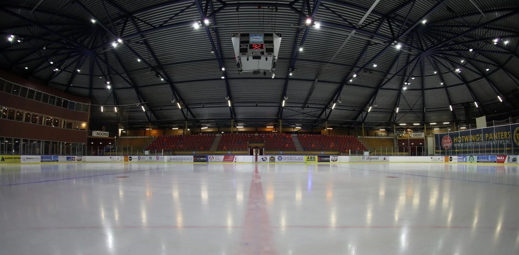 De lege ijshockeybaan van 30 bij 60 meter gezien vanaf het ijs, met het koepeldak en de tribunes erachter – SilverDome