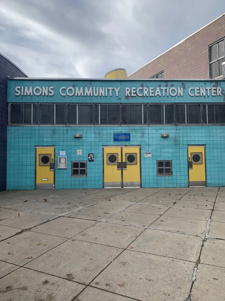 The turquoise front of the Simons Community Recreation Center with its name along the top and yellow entrance doors. — Simons Ice Rink