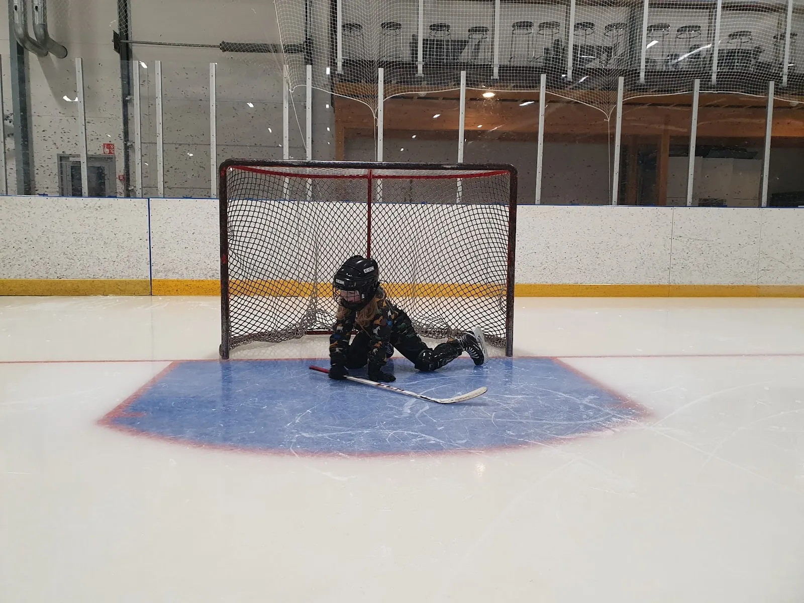 The ice at Sini-areena in Posio with a goal, crease and rink boards, a player in the net — Sini-areena
