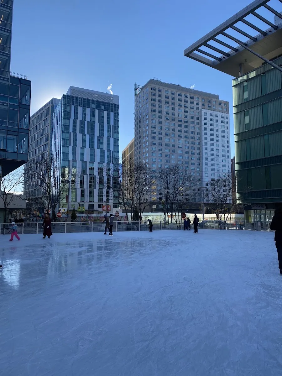 The open-air rink at Canal District Kendall in daylight with a few skaters under the surrounding office towers. — Skate @ Canal District Kendall