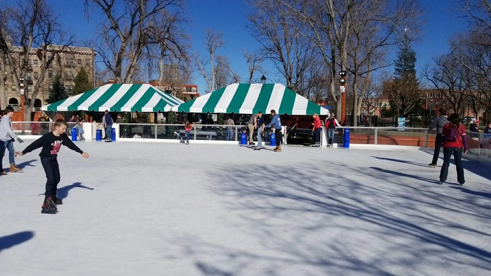The outdoor ice rink at Acacia Park under green-and-white striped tents with a skater on the ice (Google Maps listing photo) — Skate in the Park at Acacia Park