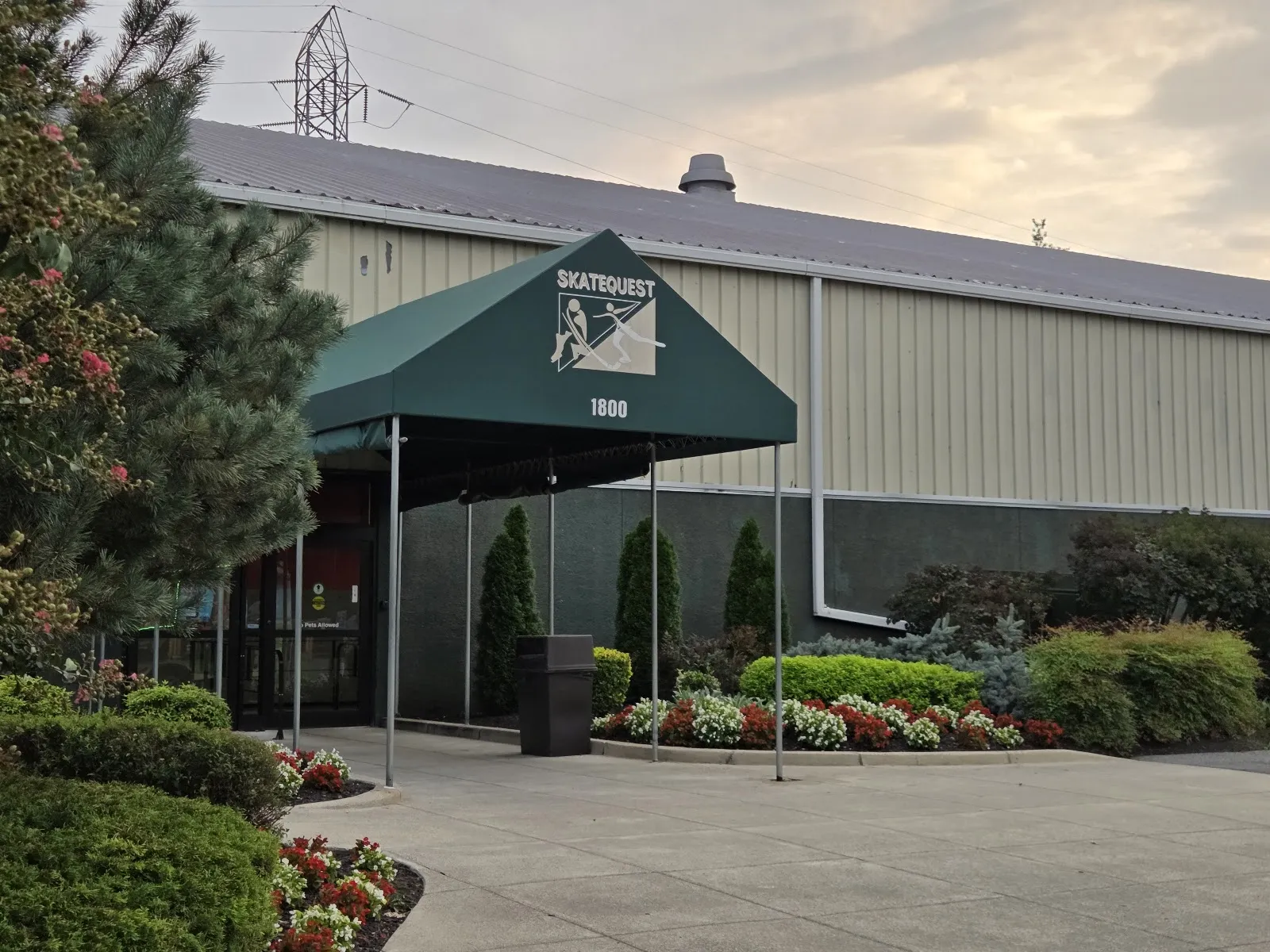 Front entrance of the beige metal building under a green awning reading SKATEQUEST with the address number 1800, landscaped walkway in front — SkateQuest (Reston)