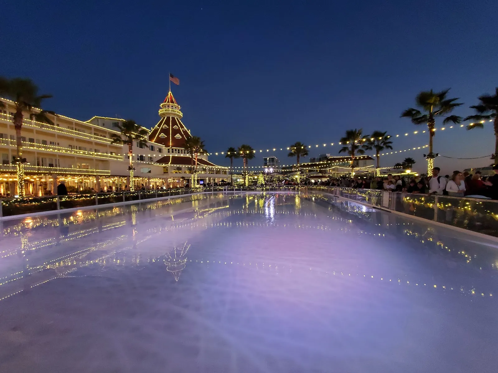 The beachfront rink at dusk, its lit surface reflecting the strings of lights along the Victorian hotel and its red-roofed tower. — Skating by the Sea (Hotel del Coronado)