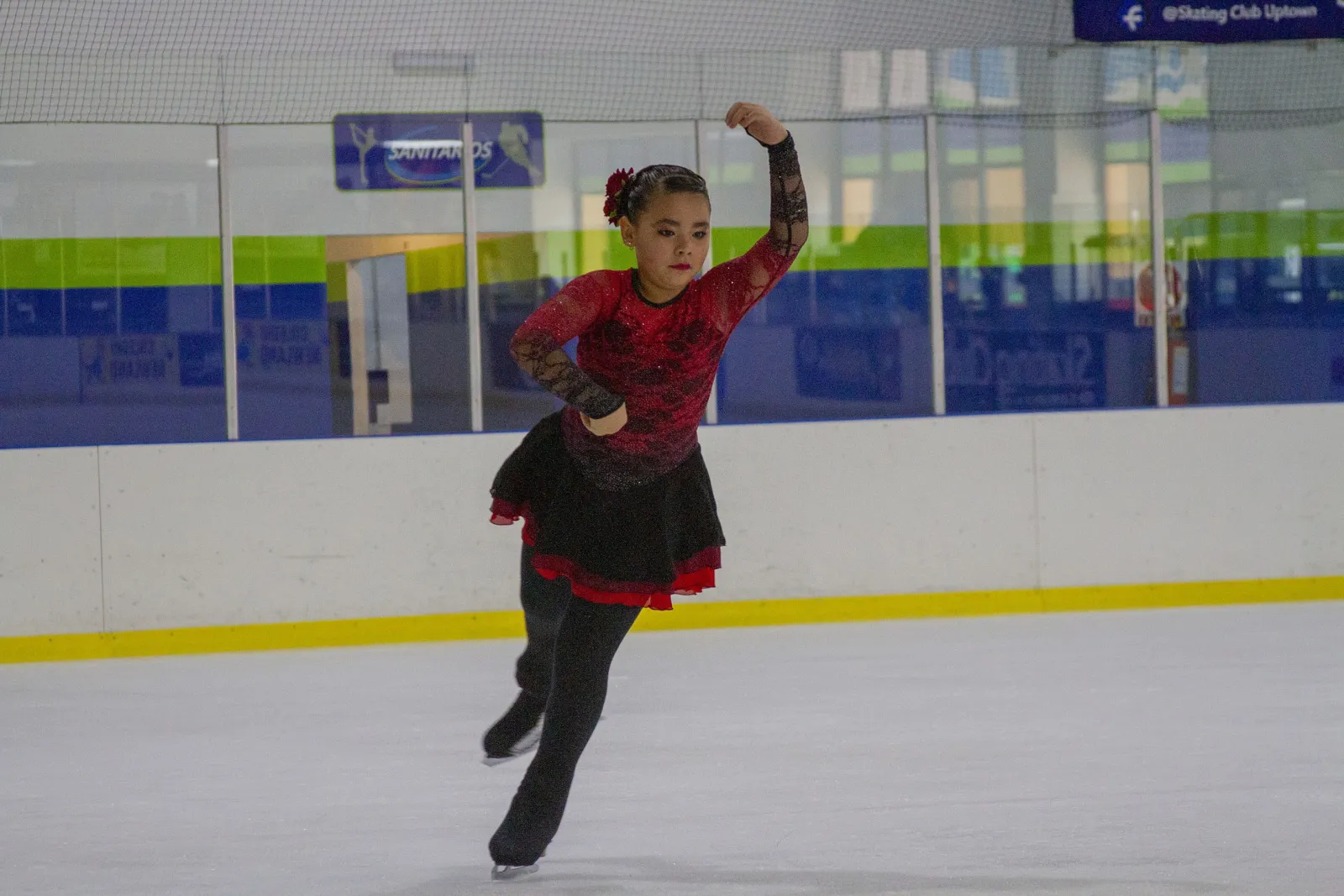 Una patinadora practicando un giro sobre el hielo en Skating Club Uptown, con las bandas y la pared de la arena detrás de ella. — Skating Club UpTown