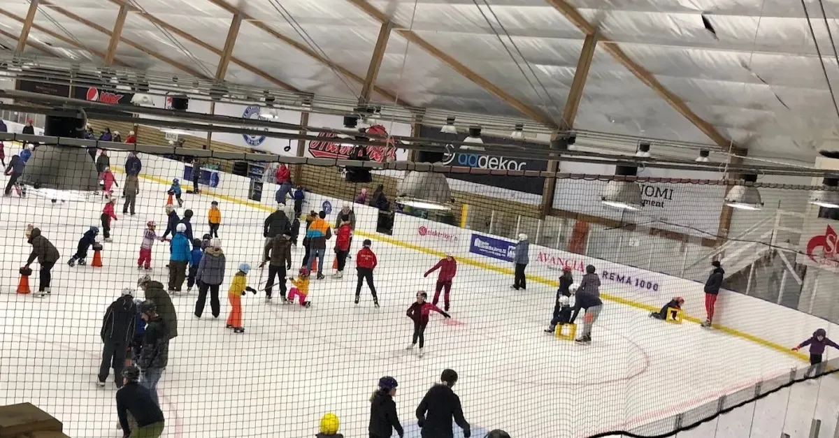 A public skating session in the Skedsmo ice hall, skaters scattered across the ice under the timber-trussed roof. — Skedsmo Ishall