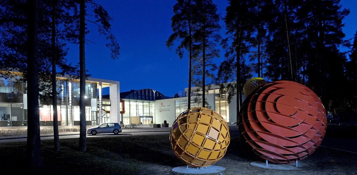 Skien Fritidspark at dusk, with the park's entrance building behind two large sculptures. — Skien Fritidspark skøytebane