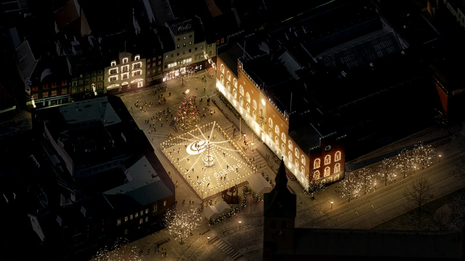 Et luftfoto af Flakhaven i Odense om natten, hvor skøjtebanen er oplyst i et stjernemønster på den åbne plads, med oplyste bygningsfacader langs siderne og julelys i træerne. — Skøjtebanen på Flakhaven