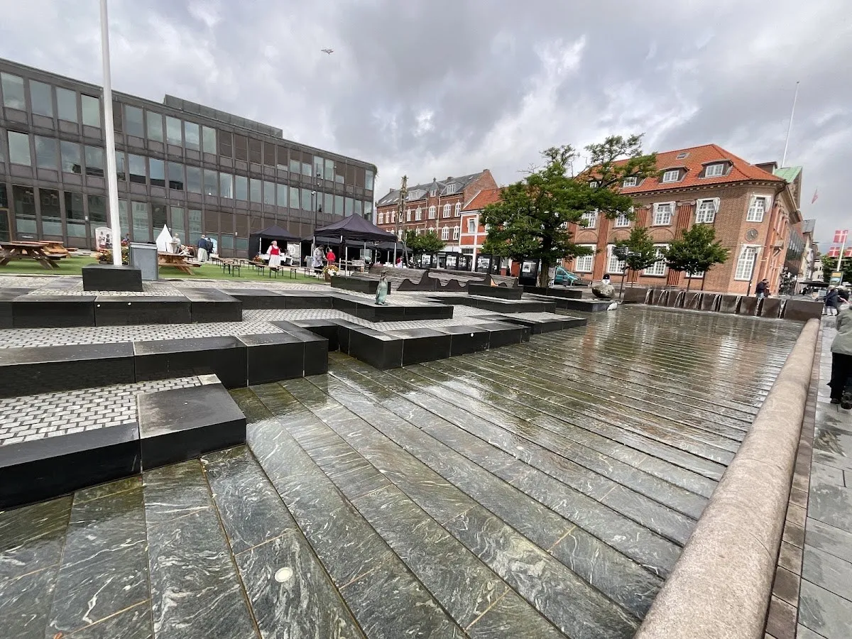 Rådhuspladsen i centrum af Fredericia, den stenbelagte plads med et vandelement og rådhusbygningerne bagved, hvor vinterens skøjtebane opstilles (fotoet viser pladsen om sommeren uden skøjtebanen) — Skøjtebanen på Rådhuspladsen