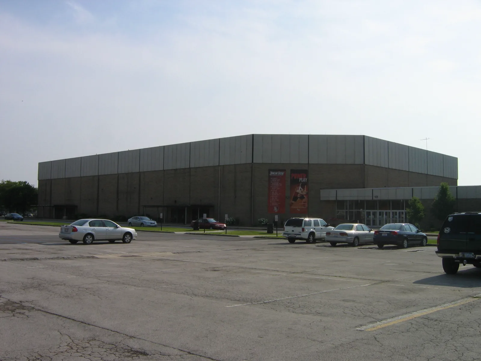 Arena's long windowless grey precast wall rising above its surface parking — Slater Family Ice Arena