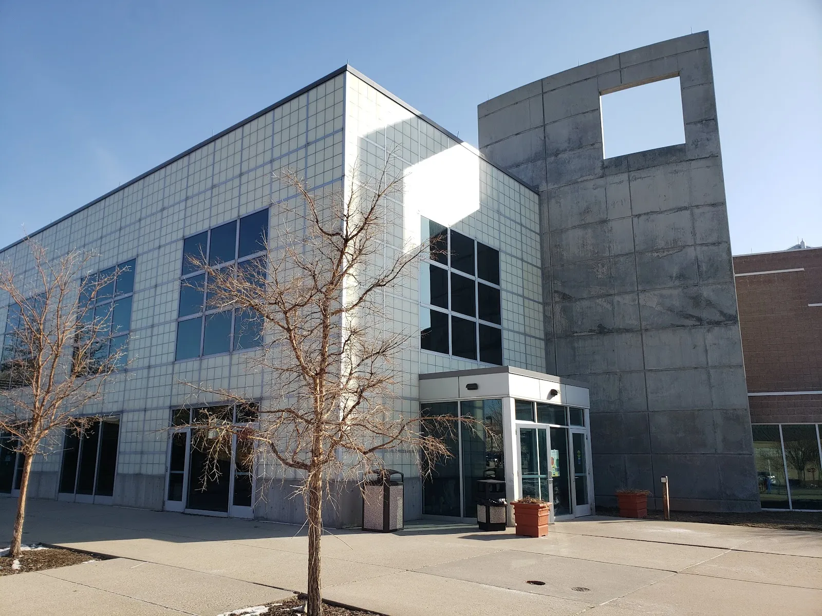 La entrada de vidrio en la esquina del edificio, junto a una alta torre de concreto con una abertura cuadrada cerca de la parte superior. — Salt Lake City Sports Complex