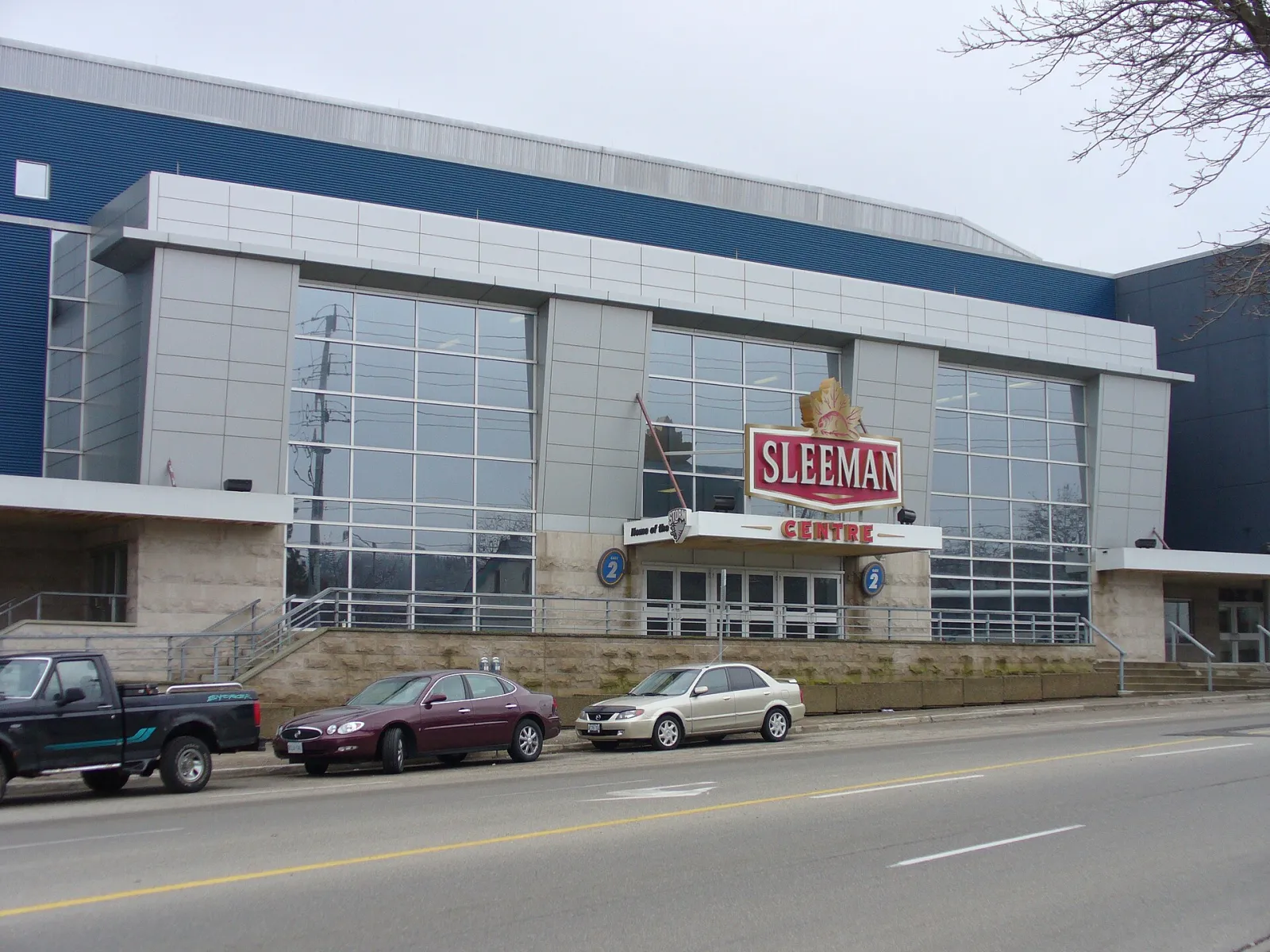 El frente de vidrio y paneles azules del Sleeman Centre en Woolwich Street, con el letrero de Sleeman sobre la entrada. — Sleeman Centre