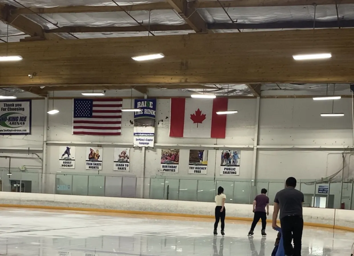 Public skating at the Sno-King Kirkland rink below the wooden roof beams, with the flags, program banners and Raise the Rink sign on the end wall — Sno-King Ice Arenas - Kirkland