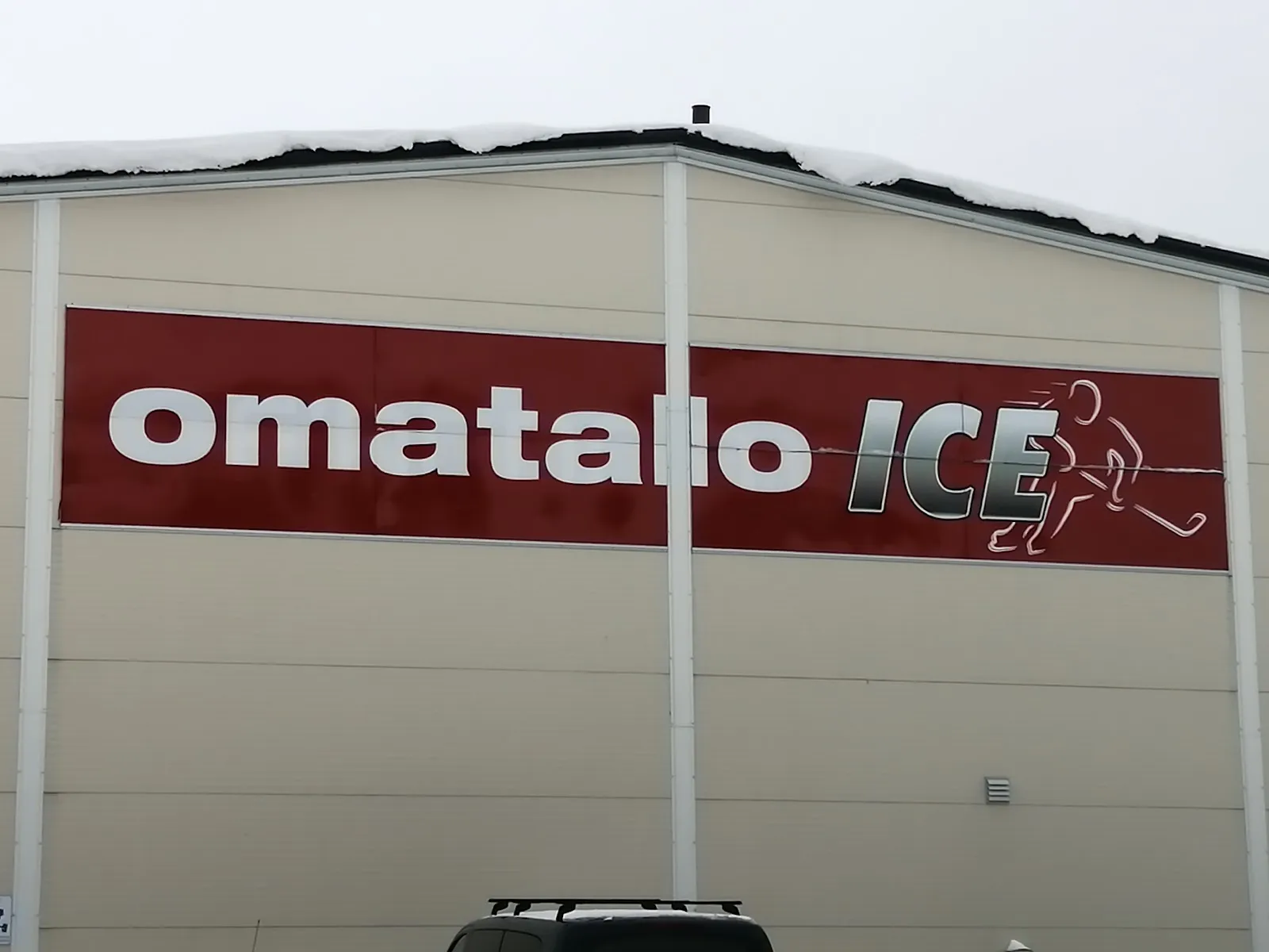 The pale metal end wall of the Sonkajärvi ice hall with the Omatalo ICE sign across it. — Sonkajärven jäähalli