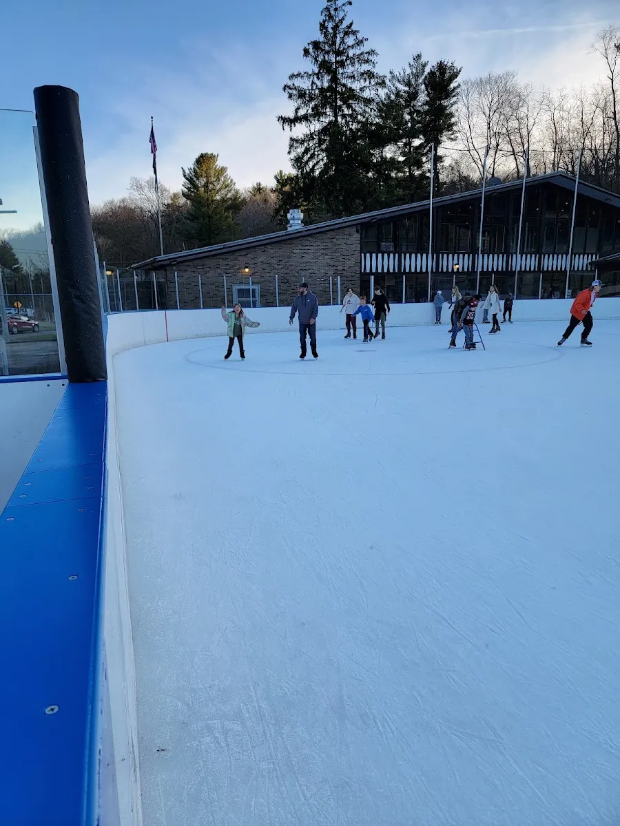 The rink lodge, a long brick building with dark timber gables, seen across the ice from a corner of the boards on a clear late afternoon. — South Park Ice Rink