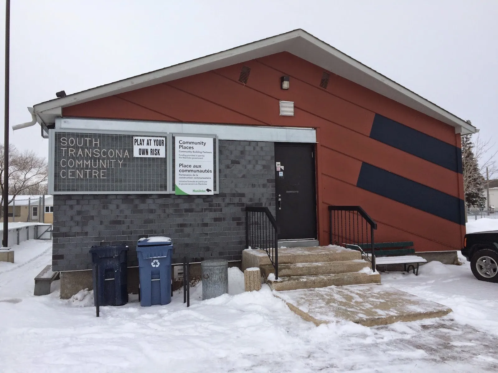 El South Transcona Community Centre en invierno, un pequeño edificio de ladrillo y revestimiento rojo con el letrero del centro junto a la puerta — South Transcona Community Centre Outdoor Rink