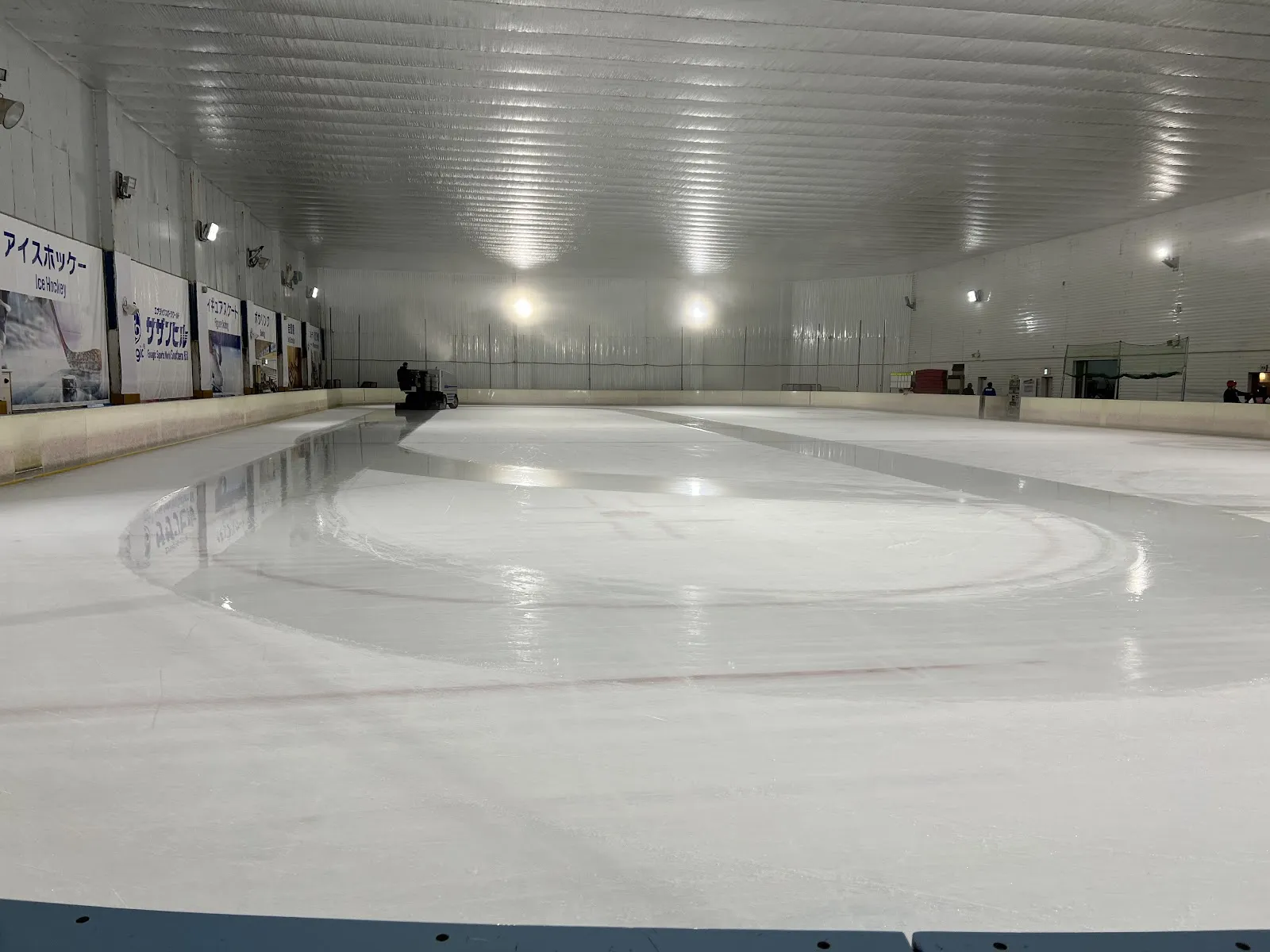 The empty ice of Southern Hill Ice Arena under its low silver ceiling, with the resurfacer at the far end and the sponsor boards along the wall. — Southern Hill Ice Arena