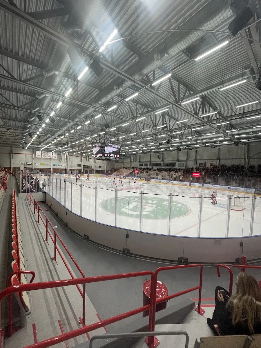 The ice sheet inside Ljungby Arena seen from the stand, with the red railings and the green centre logo – SP Arena (ishallarna), Ljungby