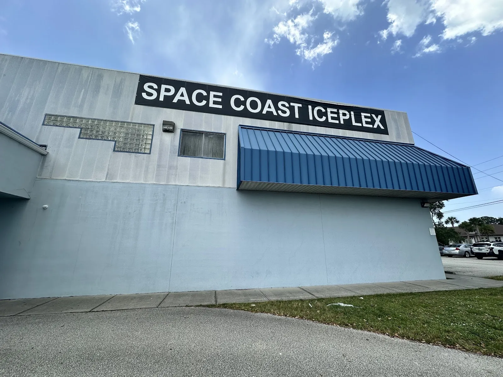The Space Coast Iceplex building, its name on a black banner along the pale blue wall above a blue metal awning — Space Coast Iceplex