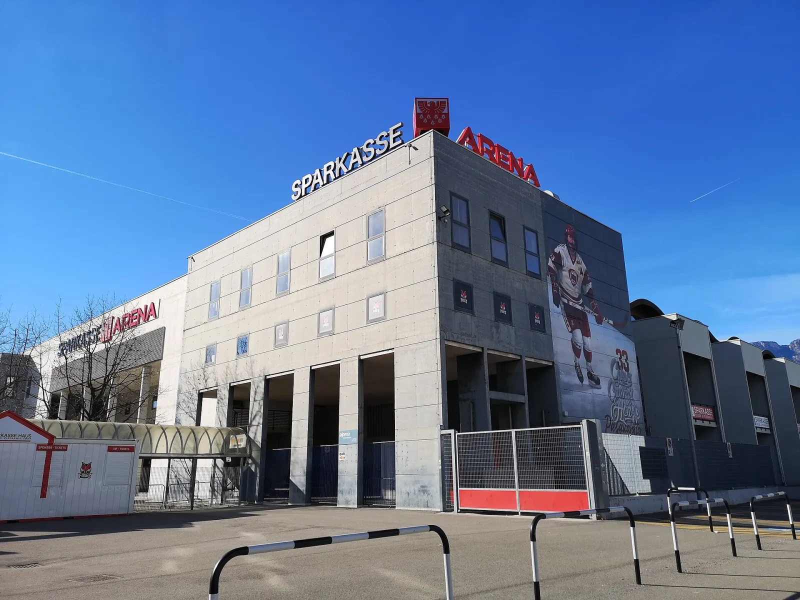 The Sparkasse Arena in Bolzano seen from the street, with the arena name on the roof and a hockey player mural on the side wall. — Sparkasse Arena (Palaonda)