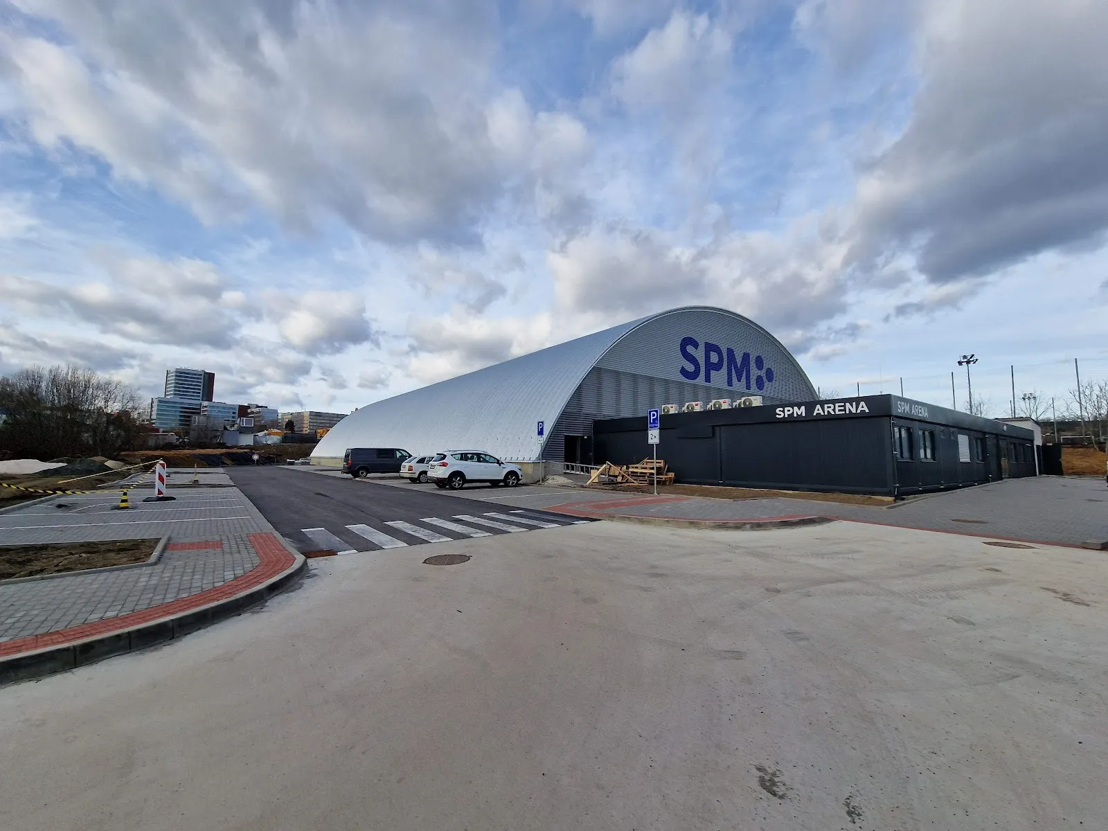 Budova SPM Areny s obloukovou střechou a nápisem u vchodu v Praze 5 – SPM Arena
