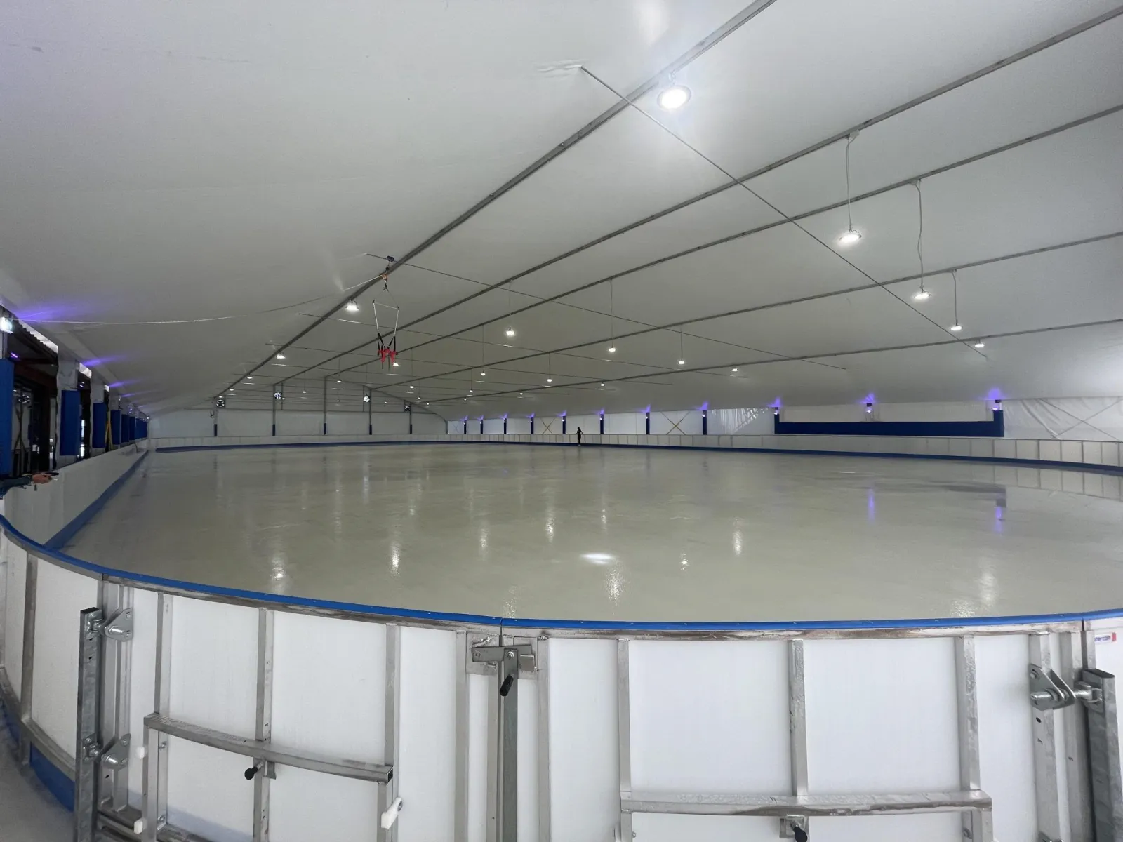 The empty ice sheet seen from beside the boards, under the white ceiling of the tent structure. — Sporting Club Panda (pista di pattinaggio)