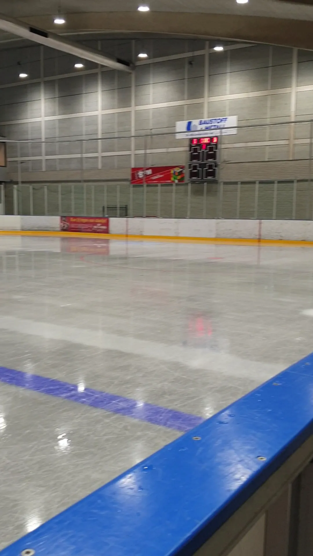 The empty ice along the blue boards at Sportiom, with the scoreboard and the pale hall wall behind — Sportiom