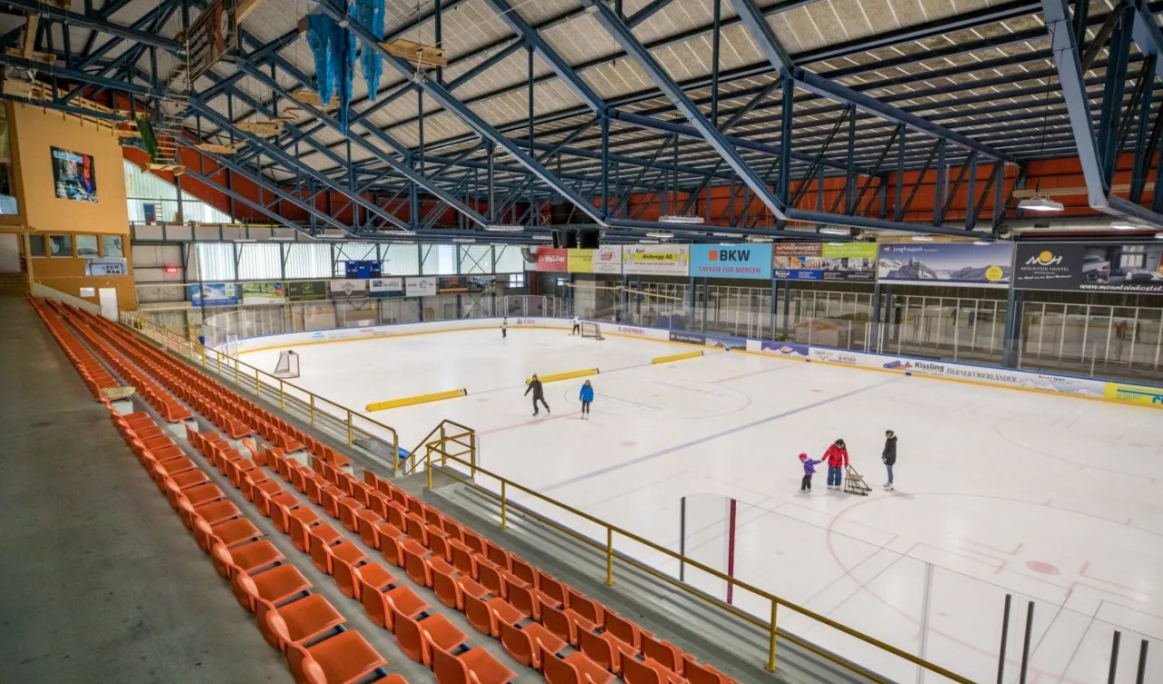 The ice surface of the Eishalle seen from the grandstand, with a few skaters on the ice — Sportzentrum Grindelwald
