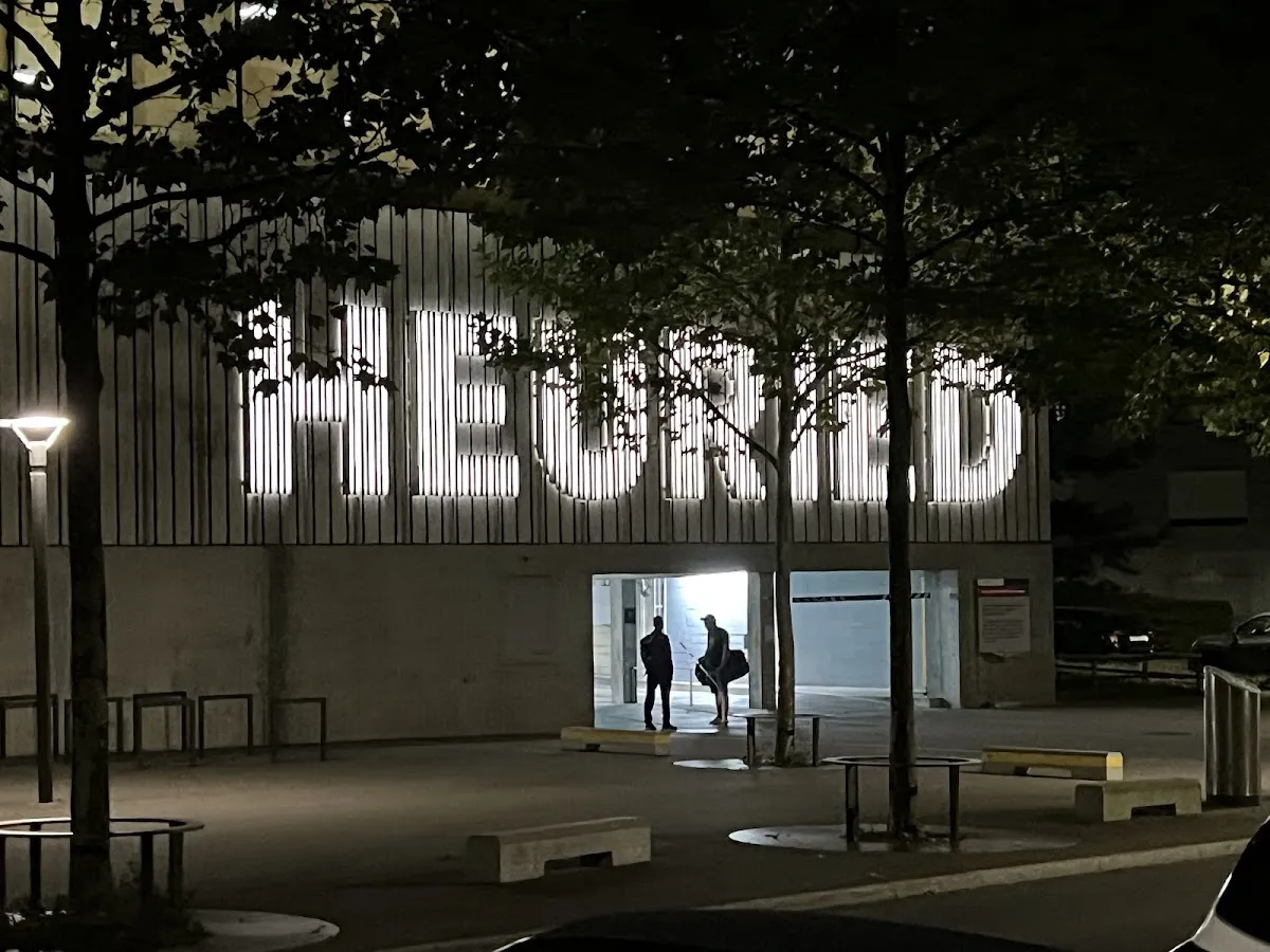 The illuminated HEURIED lettering above the entrance of the Sportzentrum Heuried in Zürich in the evening — Sportzentrum Heuried
