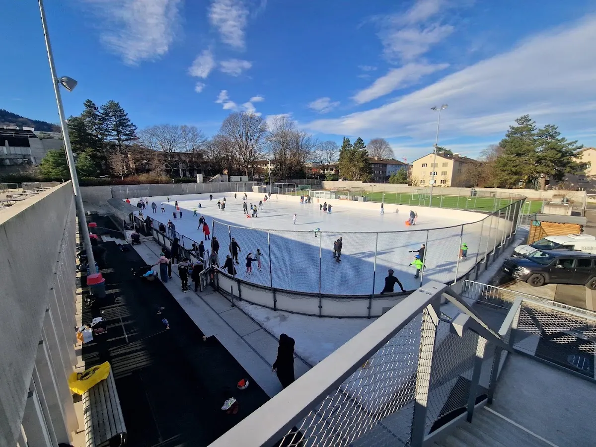 The open-air ice of the Sportzentrum Heuried in Zürich on a sunny day, seen from the walkway above, with public skaters on the surface — Sportzentrum Heuried