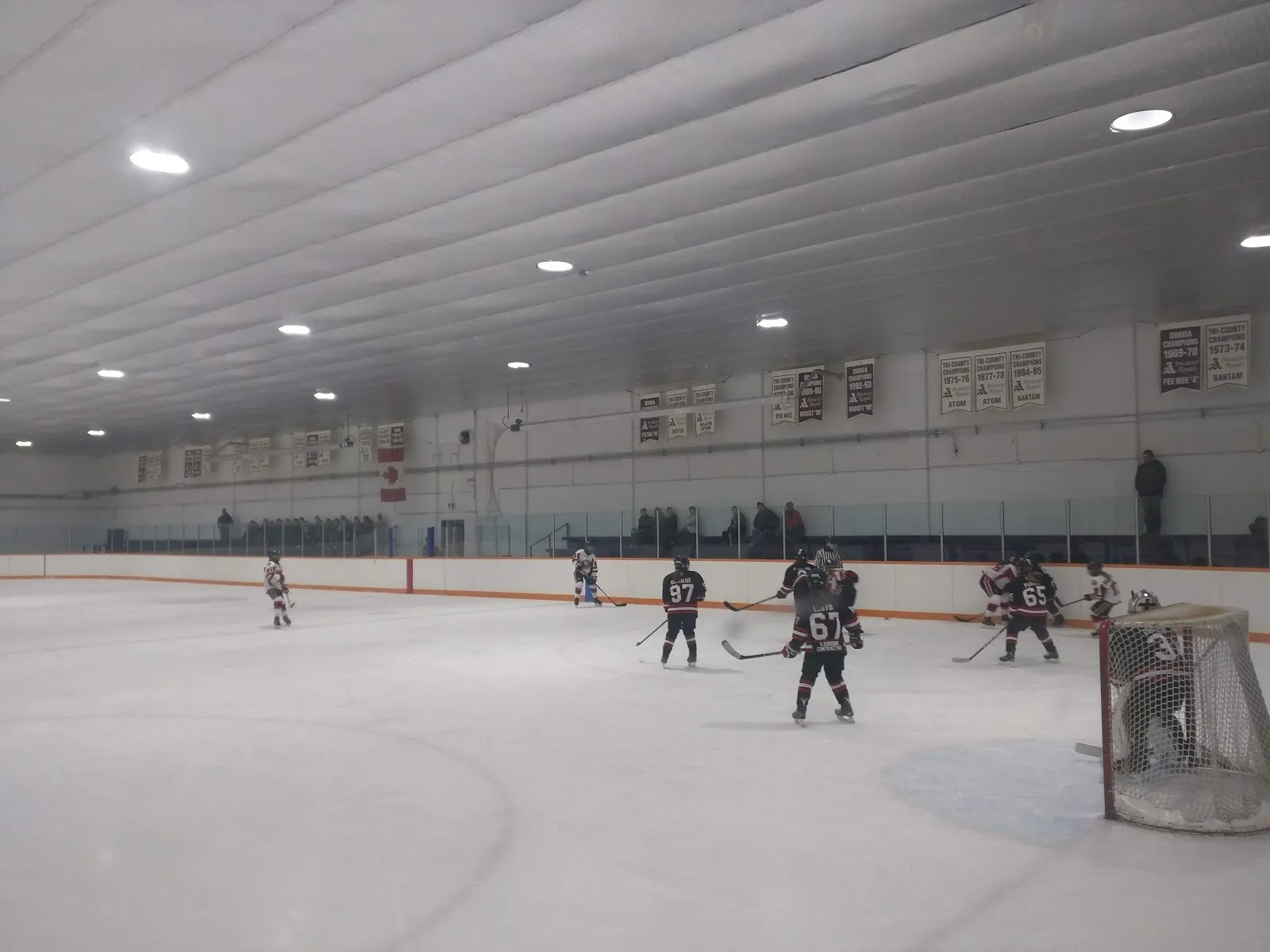 Un partido visto a lo largo de las vallas, con jugadores repartidos por una pista amplia y clara bajo un techo blanco acanalado. — Spring Valley Arena