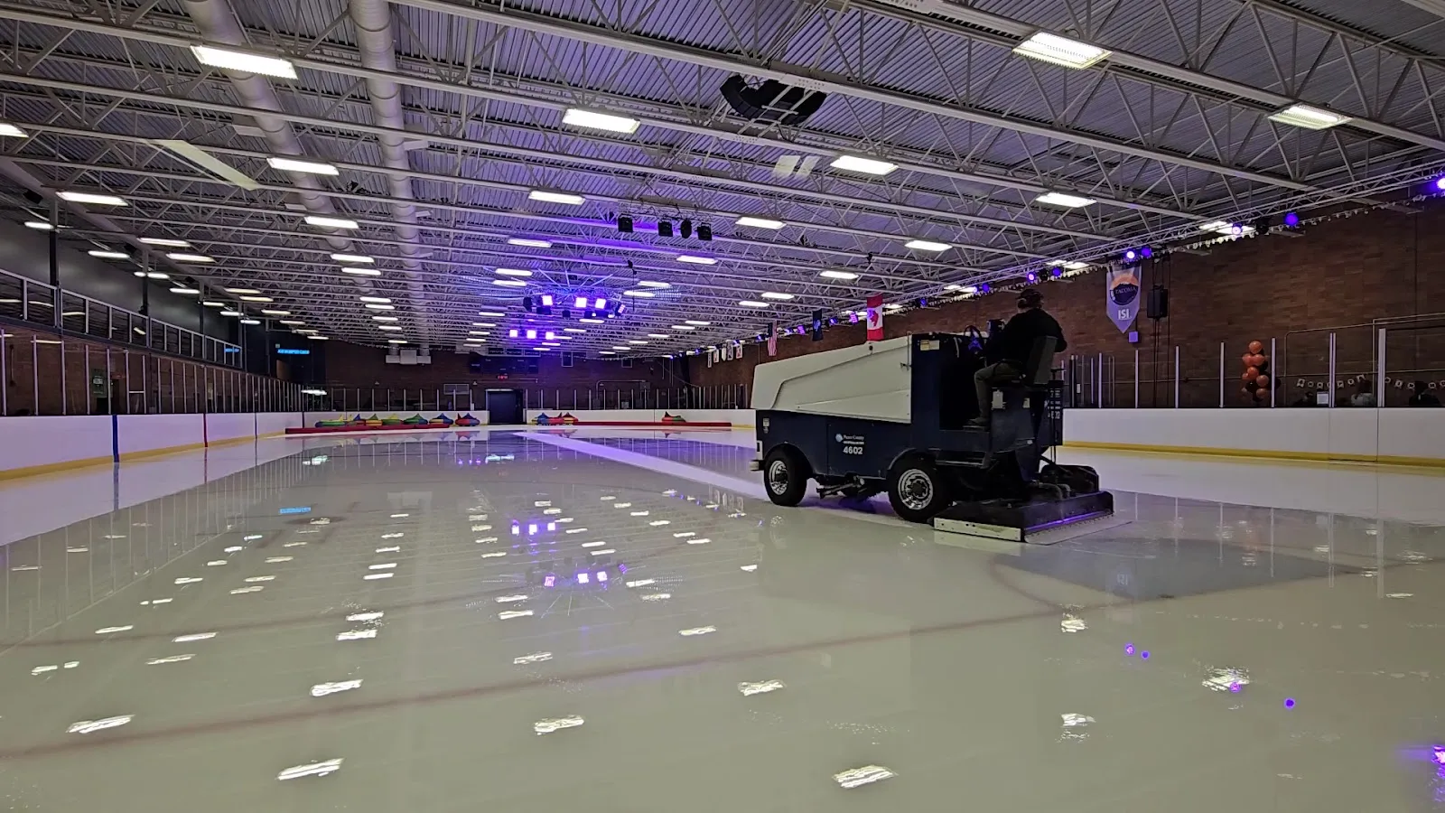 The NHL-size ice with the resurfacer at work and coloured stage lights above the boards. — Sprinker Recreation Center