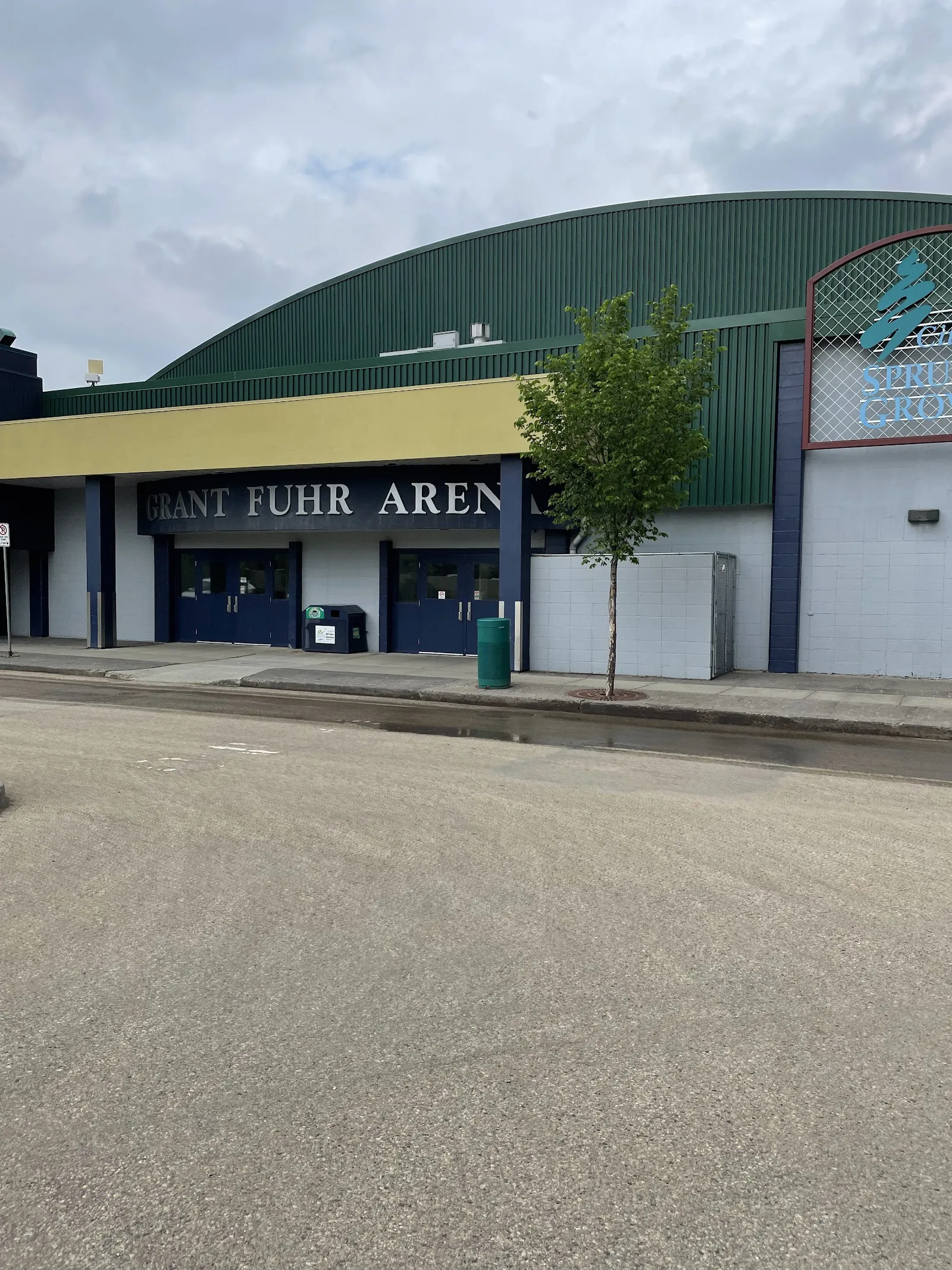 El frente verde de techo curvo de Grant Fuhr Arena en Spruce Grove, con el nombre de la arena sobre las puertas, visto desde el estacionamiento — Spruce Grove Agrena