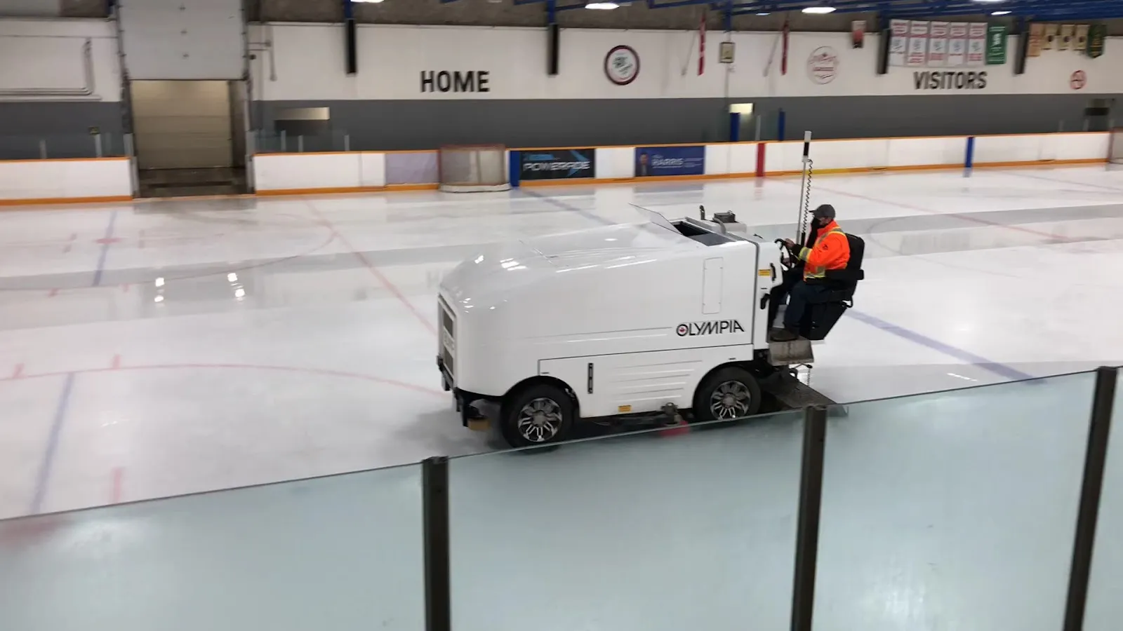 An ice resurfacer crossing the rink, with "Home" and "Visitors" lettering on the far wall and the boards in the foreground. — St. Jacobs Arena