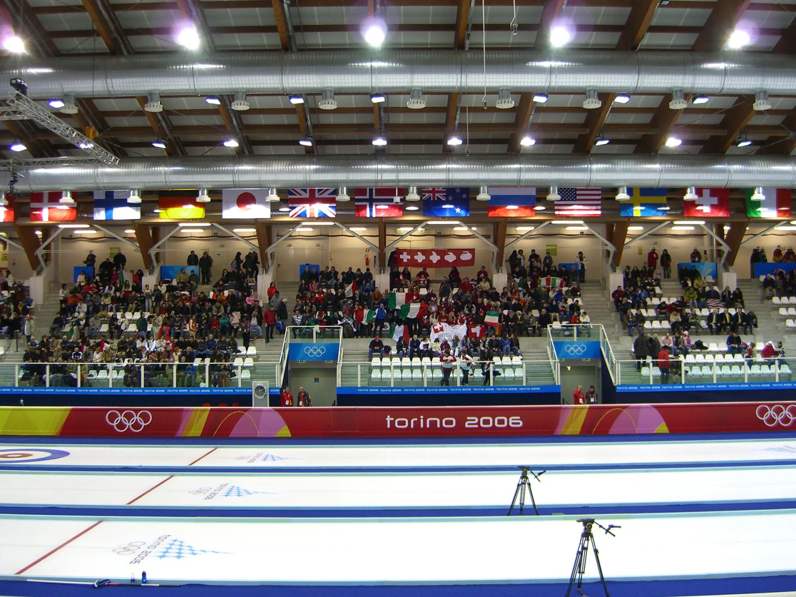 Il ghiaccio e le tribune della sala di Pinerolo, fotografati nel febbraio 2006 durante il torneo olimpico di curling, con le piste di ghiaccio davanti alle tribune e il tetto in legno sopra. – Stadio Olimpico del Ghiaccio (Ice Pole Pinerolo)
