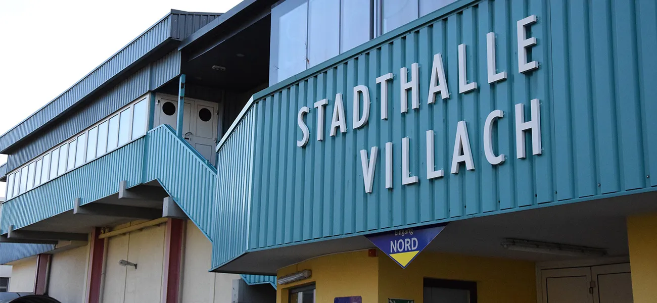 Die türkisfarbene Metallfassade der Stadthalle Villach mit dem Namen in erhabenen Buchstaben und dem Schild „Nord“ über der Eingangstreppe – Stadthalle Villach