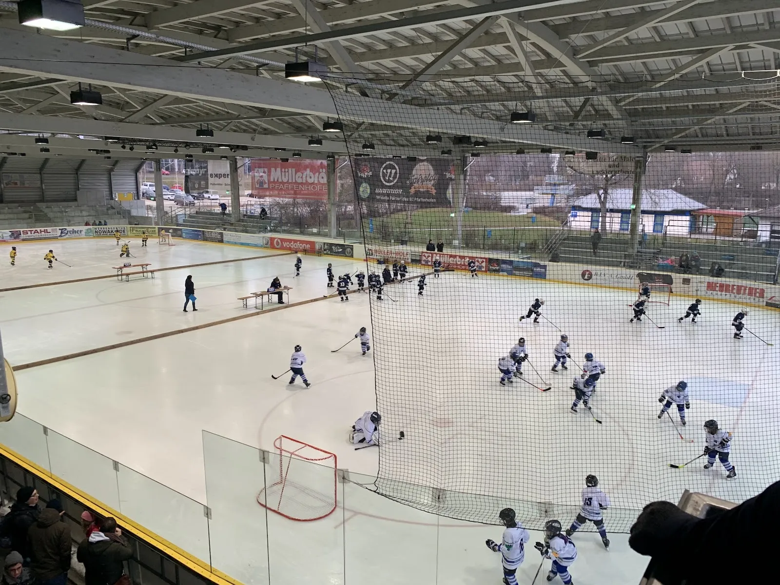A youth game on the ice of the Stadtwerke-Arena in Pfaffenhofen, seen from above the boards across the sheet. — Stadtwerke-Arena Pfaffenhofen