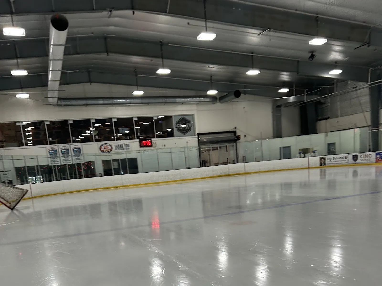 Empty ice at Stamford Twin Rinks from rink level, looking toward the boards and the lounge windows above them — Stamford Twin Rinks