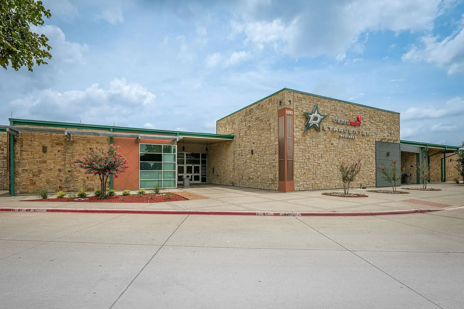 Piedra y estuco desde el estacionamiento, con detalles verdes a lo largo de la entrada — Children's Health StarCenter McKinney
