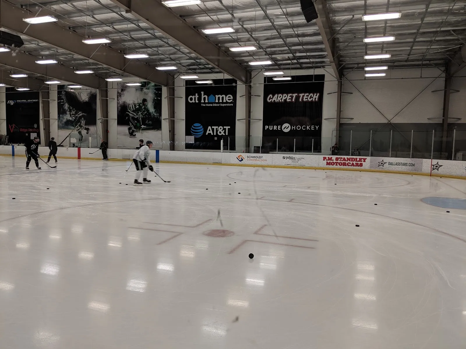 Una práctica en una pista de StarCenter McKinney, vista desde el vidrio con las mantas de patrocinadores y las vallas de los Dallas Stars al fondo — Children's Health StarCenter McKinney