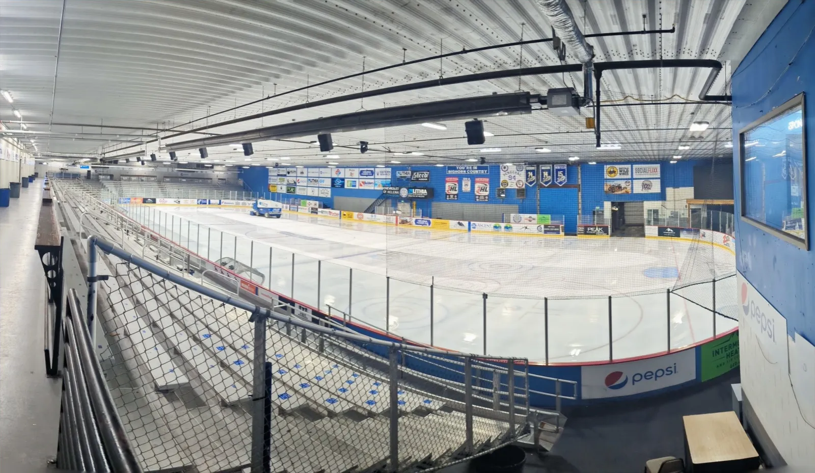 The empty ice at Steed Arena in a wide view from the upper walkway, with the stand and the boards along the side — Steed Arena