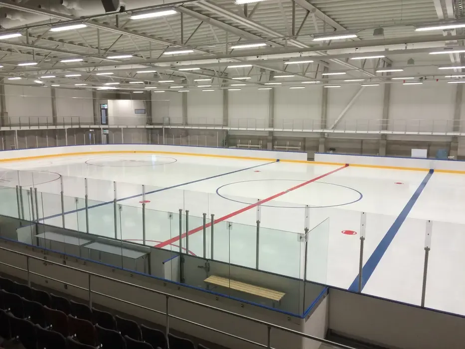 The empty ice sheet of the Stenungsund Arena ice hall seen from the stands, with the blue and red lines, face-off circles, glass-topped boards and the upper walkway behind. – Stenungsund Arena (ishall)
