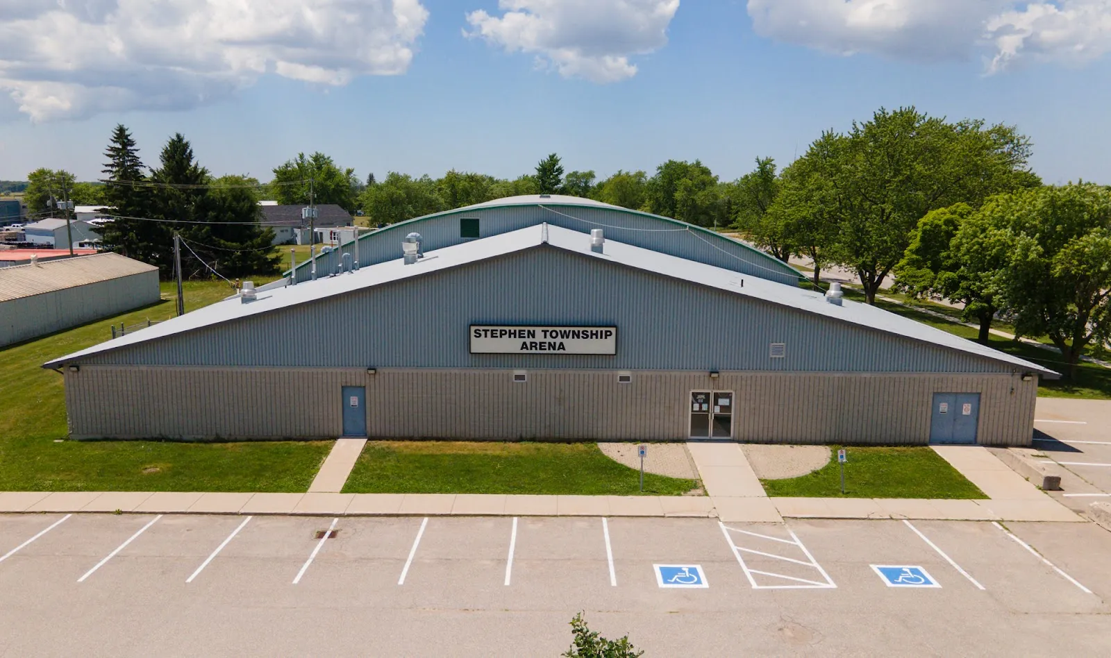 The long blue-grey Stephen Township Arena with its name sign over the front doors and accessible parking. — Stephen Township Arena (Huron Park)