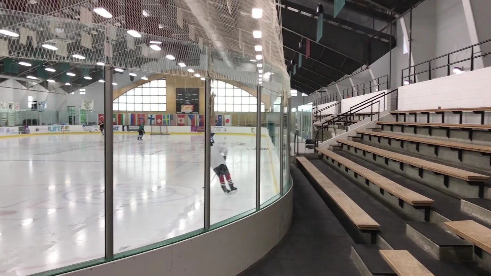 The ice sheet at Stephen C. West Ice Arena, with glass and tiered bleachers along one side and a lone skater at the far end. — Stephen C. West Ice Arena