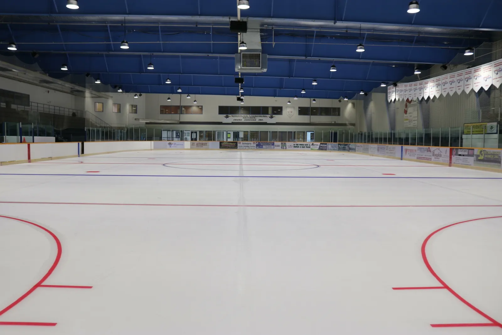 The empty ice sheet at the Stettler Recreation Centre arena, with blue roof trusses and banners above the far boards — Stettler Recreation Centre