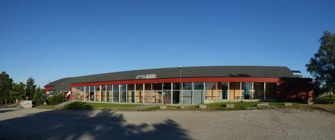 Stjernehallen sett fra parkeringsplassen en klar dag: den lange, lave ishallen med rød og oransje fasade. — Stjernehallen