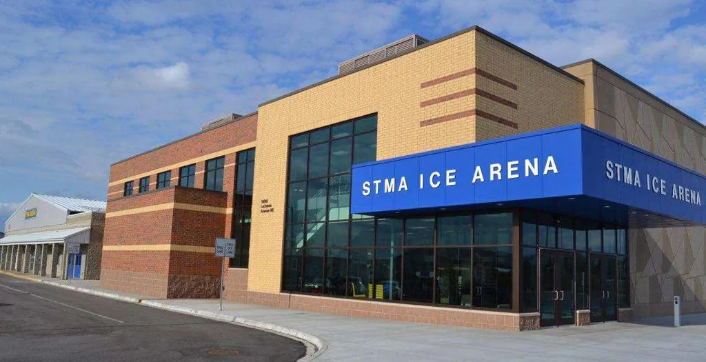 Front exterior of the STMA Ice Arena building, with large blue "STMA ICE ARENA" signage over the glass entrance. — STMA Ice Arena (St. Michael-Albertville Arena)