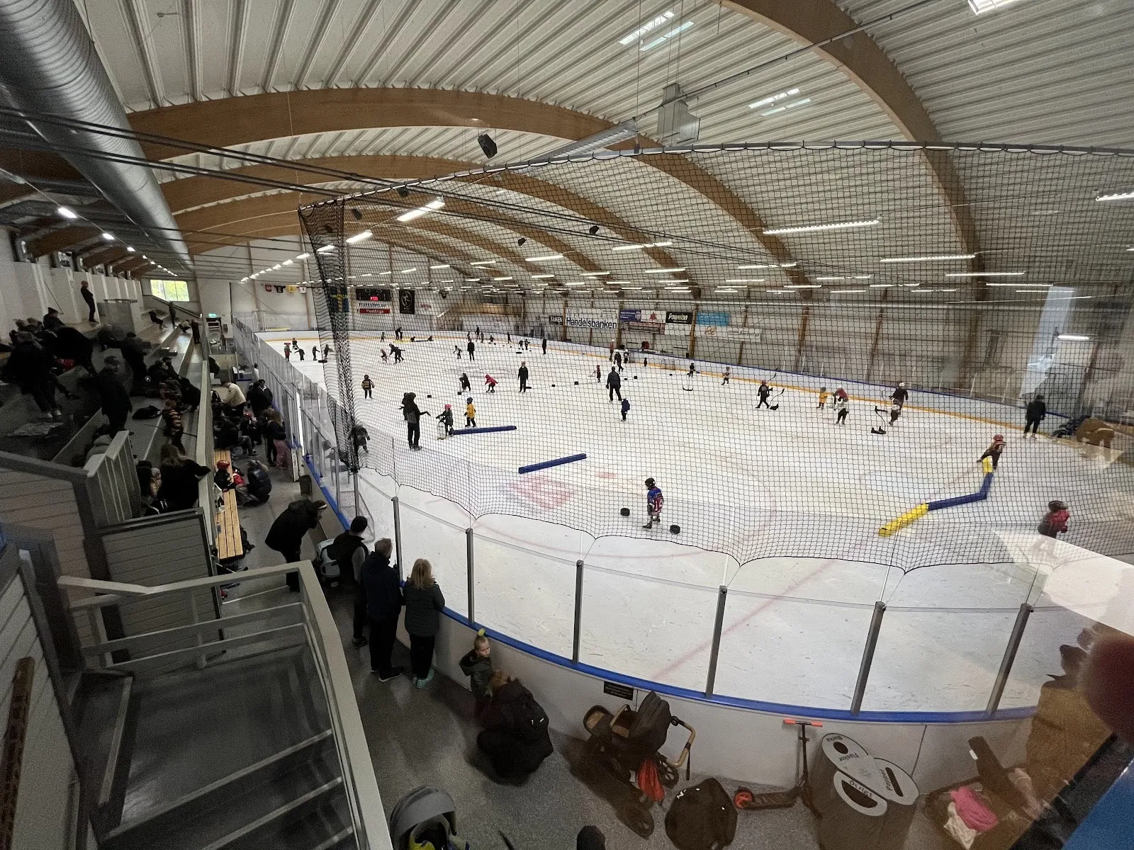 A session on the ice at Stortorpshallen, players spread across the rink with the curved wooden roof and stands above. — Stortorpshallen