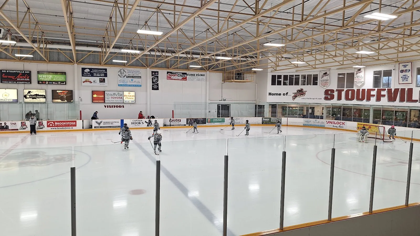 El hielo desde el nivel superior de observación, con anuncios de patrocinadores a lo largo de las paredes y una manta de Home of the Stouffville Spirit sobre las ventanas del vestíbulo. — Stouffville Arena