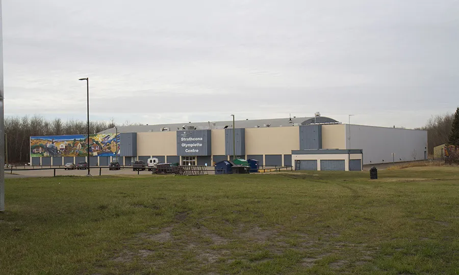 The long, low Strathcona Olympiette Centre across a grass field, a painted mural along its west wall. — Strathcona Olympiette Centre